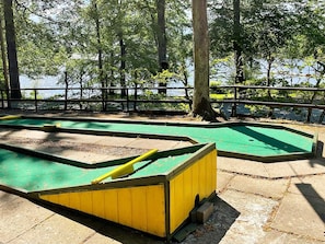Un campo de mini golf verde y amarillo, con una valla de madera y árboles al fondo.