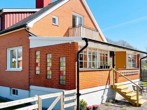 A red brick house with a white exterior trim, a wooden staircase leading to a covered porch, and a small outdoor seating area. - 4 Star Holiday Home in Sibbhult (Sibbhult)