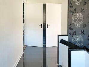 Un couloir avec une porte blanche, un mur orné d’un motif noir et blanc, et un sol carrelé.