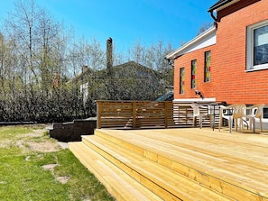 Una terraza de madera con una mesa y sillas, un edificio de ladrillo y una chimenea.