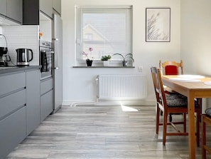 A modern kitchen with grey cabinetry, a dining table with chairs, a window with blinds, and a radiator.