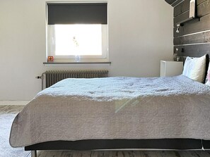 A bedroom with a bed, a radiator, a window with a view, and a shelf with items.