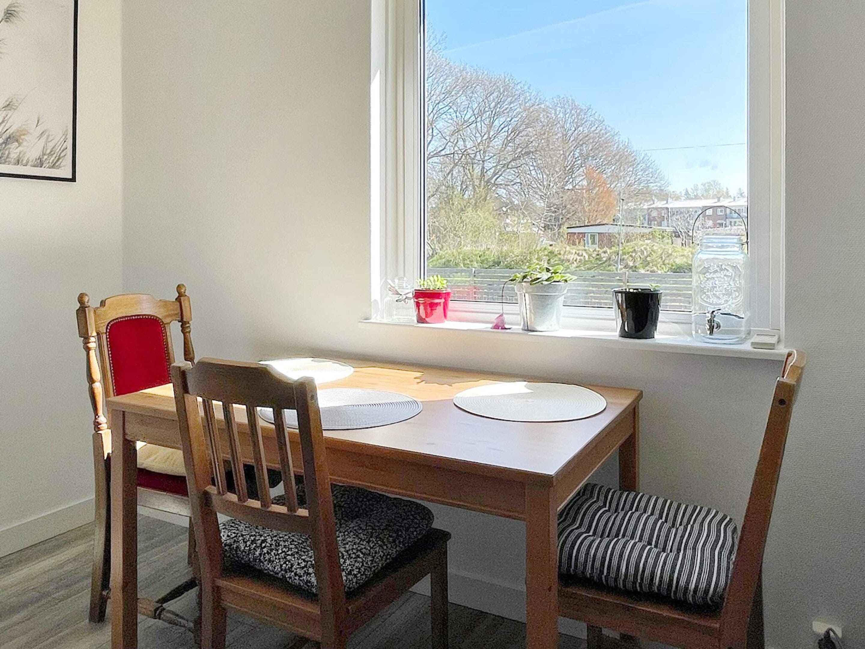 En matplats med ett träbord, två stolar och ett fönster med krukväxter.