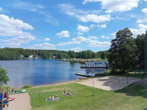 Blick auf einen See mit einem Steg, einem Boot namens MS Immel und einem Spielplatz mit Rutschen und Sandkasten.