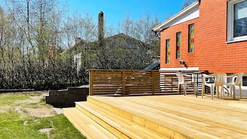 A wooden deck with outdoor seating, a brick building, and a chimney.