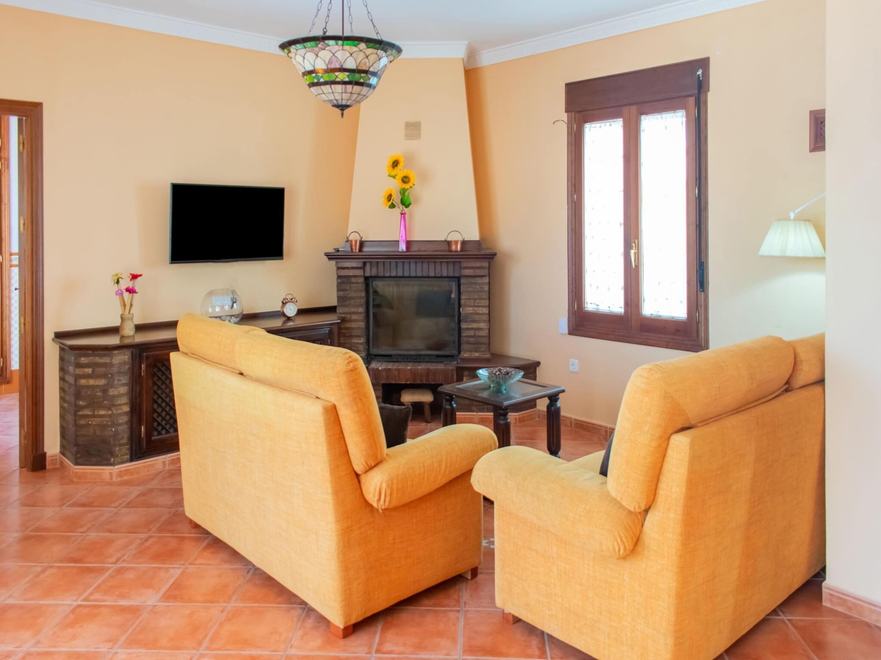 Uma sala de estar com dois sofás amarelos, uma televisão, uma lareira e uma janela.