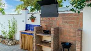 An outdoor brick barbecue area with a grill, a hanging pot, and a stone-tiled floor. - Belvilla by OYO La Ga1/4ena Vida (Algodonales)