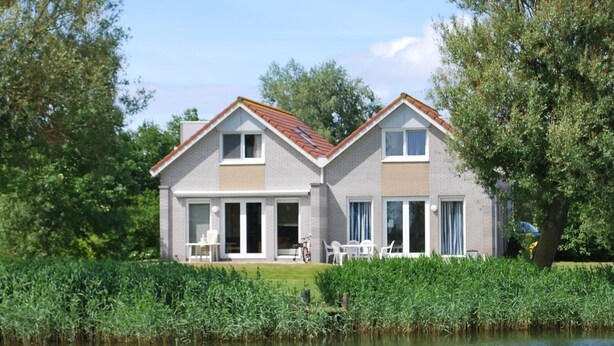 A two-story house with a sloped roof, large windows, and a patio area with outdoor furniture. - Semi-detached Bungalow on Open Water (Makkum)