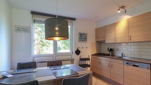 A modern kitchen with wooden cabinets, a gas stove, and a hanging pendant light. - Semi-detached Bungalow on Open Water (Makkum)
