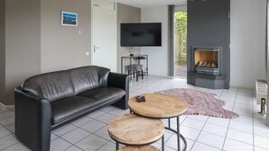 A modern living room with a leather sofa, a TV, a fireplace, and a small wooden table. - Semi-detached Bungalow on Open Water (Makkum)