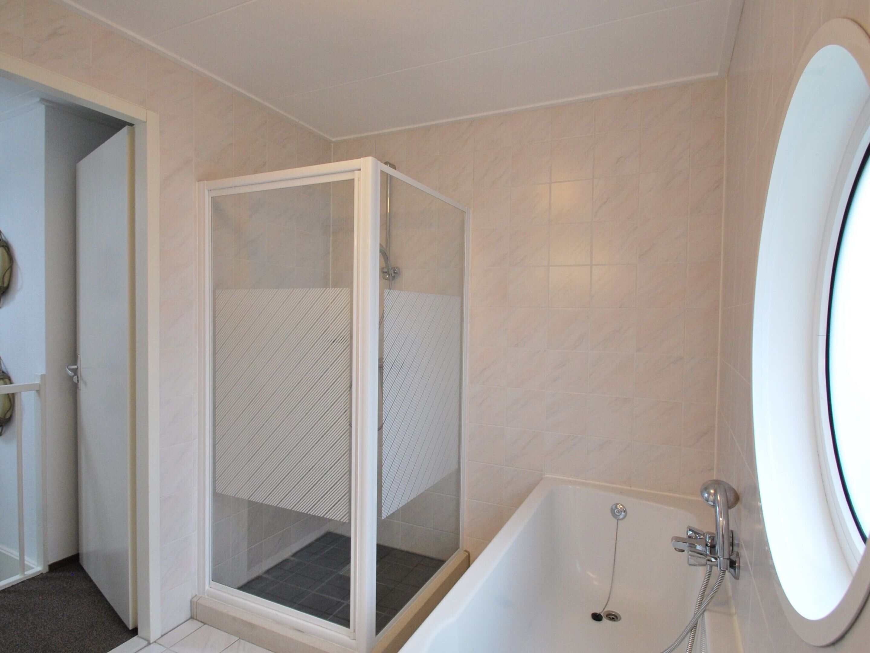 A bathroom with a glass-enclosed shower, a bathtub with a handheld showerhead, and a large mirror.