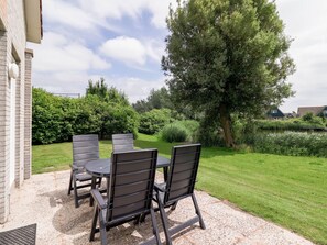 An outdoor patio with a table and four chairs, surrounded by a well-maintained lawn and trees. - Nice Holiday Home on the Water in Friesland (Makkum)