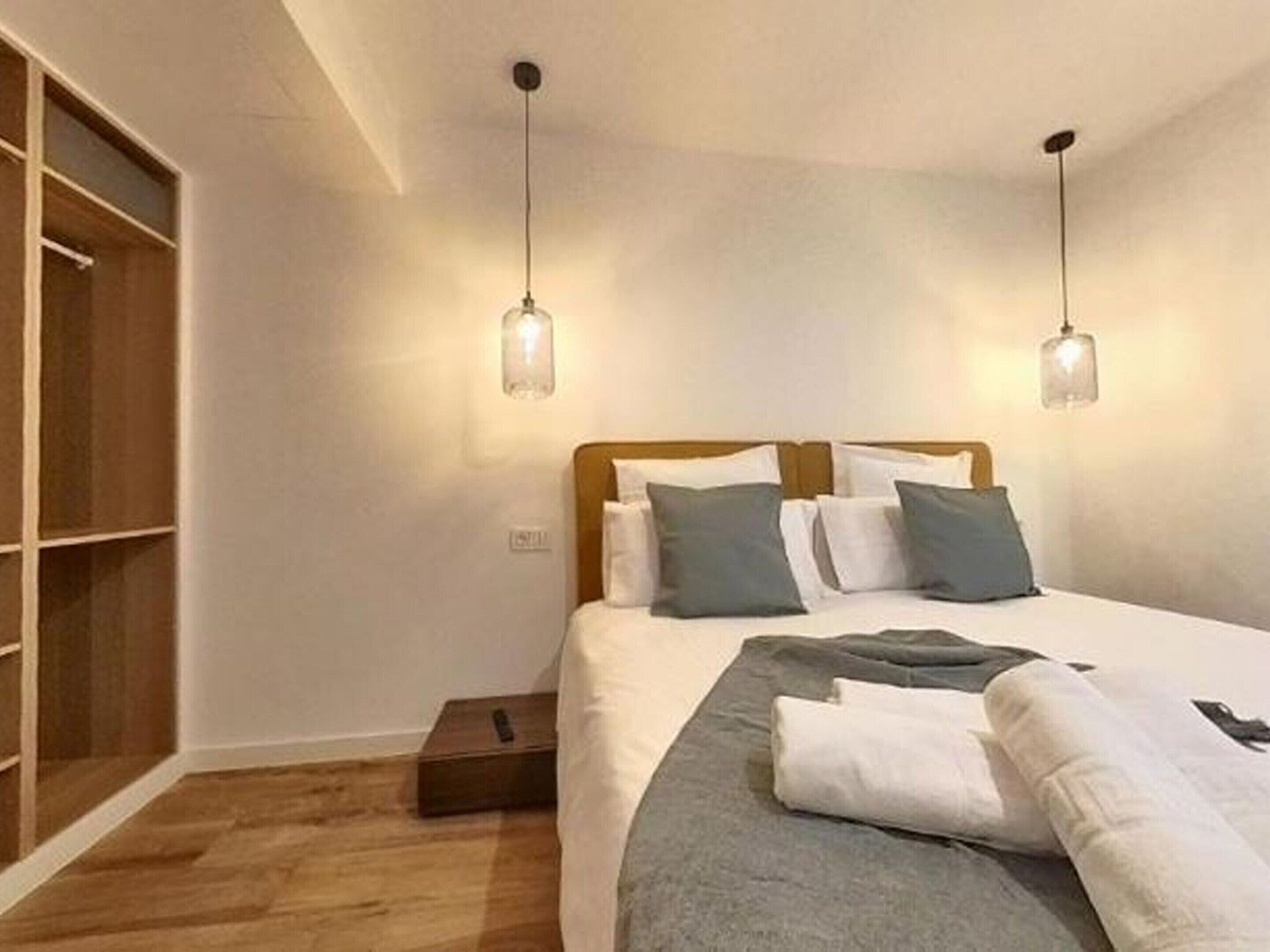 A neatly made bed with a wooden headboard, two bedside lamps, and a wooden wardrobe to the left.