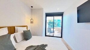 Un dormitorio con cama, una lámpara en el techo, un televisor montado en la pared y un ventanal corredero que da a un espacio al aire libre.