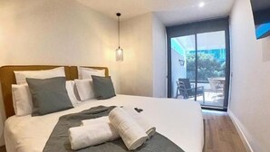 Una habitación de hotel con cama, almohadas, una manta y vistas a través de un ventanal.
