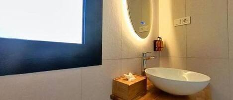 Un baño moderno con un espejo ovalado grande, un lavamanos blanco y un mueble de tocador de madera.