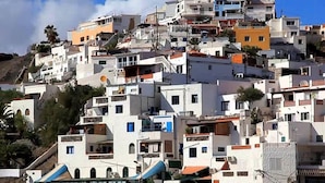 Un pueblo costero con edificios blancos, algunos con balcones, y un restaurante en la parte baja.