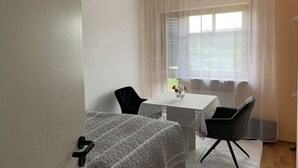 Una habitación con una cama, una mesita con un florero y una silla.