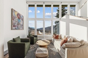 A living room with a large window, a green armchair, a beige sofa, and a wooden coffee table. - Rustic Mountainside 5 Bdrm Ski Home w/ Stunning Views, Private Balconies and Natural Light-Filled Entertainment Space with Access to Grand Hyatt Vail (Vail)
