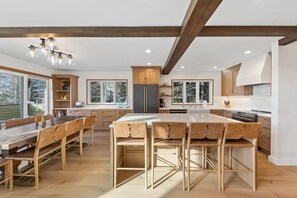 A modern kitchen with wooden beams, a central island, bar stools, and a dining table. - Rustic Mountainside 5 Bdrm Ski Home w/ Stunning Views, Private Balconies and Natural Light-Filled Entertainment Space with Access to Grand Hyatt Vail (Vail)
