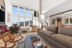 A spacious living room with a large window, a staircase, and a cozy seating area. - Newly Renovated, Luxury, Mountain Views, Ski Access Chair 20 (Vail)