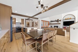 A modern kitchen with wooden cabinets, a dining area with a large table and chairs, and a living area with a sofa and fireplace. - Rustic Mountainside 5 Bdrm Ski Home w/ Stunning Views, Private Balconies and Natural Light-Filled Entertainment Space with Access to Grand Hyatt Vail (Vail)