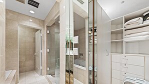 A modern bathroom with a glass shower enclosure, a built-in bathtub, and a walk-in closet with shelves for towels. - Relaxing Ski-In/Ski-Out Condo with Creek Views & Grand Hyatt Access (Vail)
