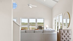Ein geräumiges Wohnzimmer mit einer großen, grauen Couch, einem Holztisch und Blick auf einen See durch große Fenster.