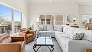 Ein geräumiges Wohnzimmer mit einer großen Eckcouch, einem Glastisch und Blick ins Freie durch große Fenster.