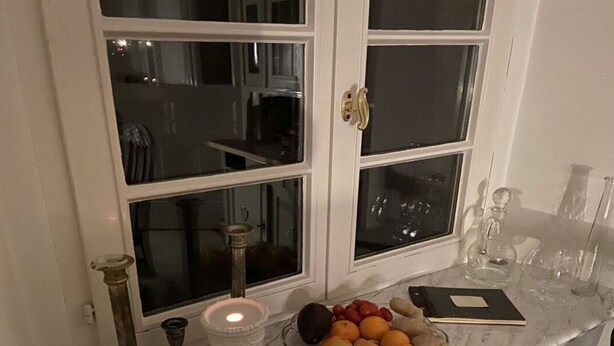 Una encimera de cocina con un frutero que contiene plátanos, naranjas y manzanas, una vela y un vaso de agua.