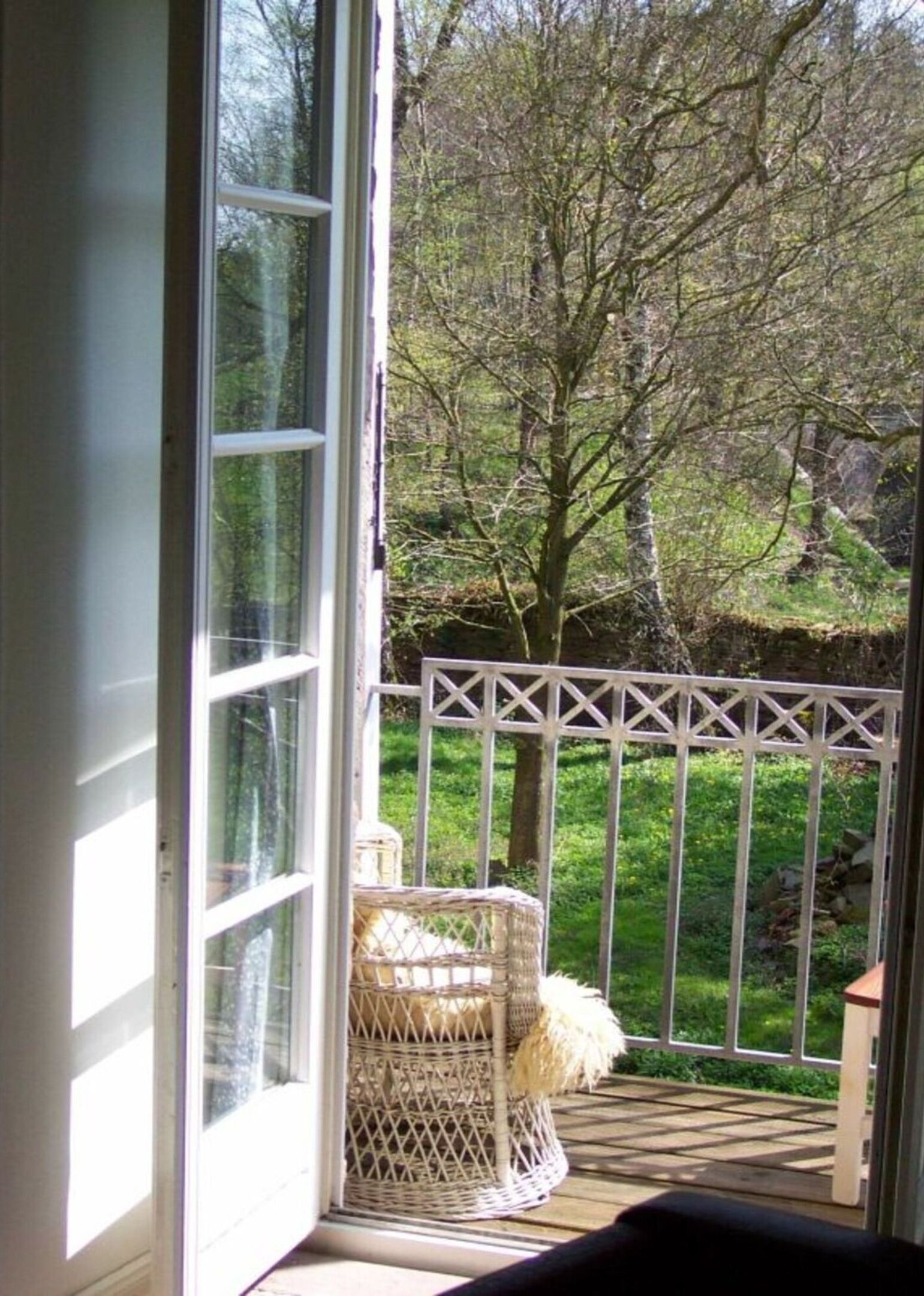 A view from a room with a large window to a deck area. The deck has a white railing and a wicker chair.