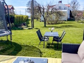 A patio with a table and chairs, a small table with a vase of flowers, and a chair with a cushion.