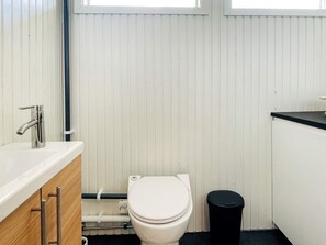 A small, compact bathroom with a white toilet, a sink, and a black trash bin.