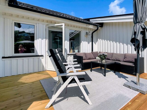 A covered outdoor seating area with a sofa and chairs, a small table with a vase, and a pergola.