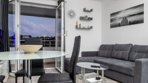 A modern living room with a grey sofa, a glass dining table, and a black chair. - Apartment Mia - Two Bedroom Apartment With Balcony (Split)