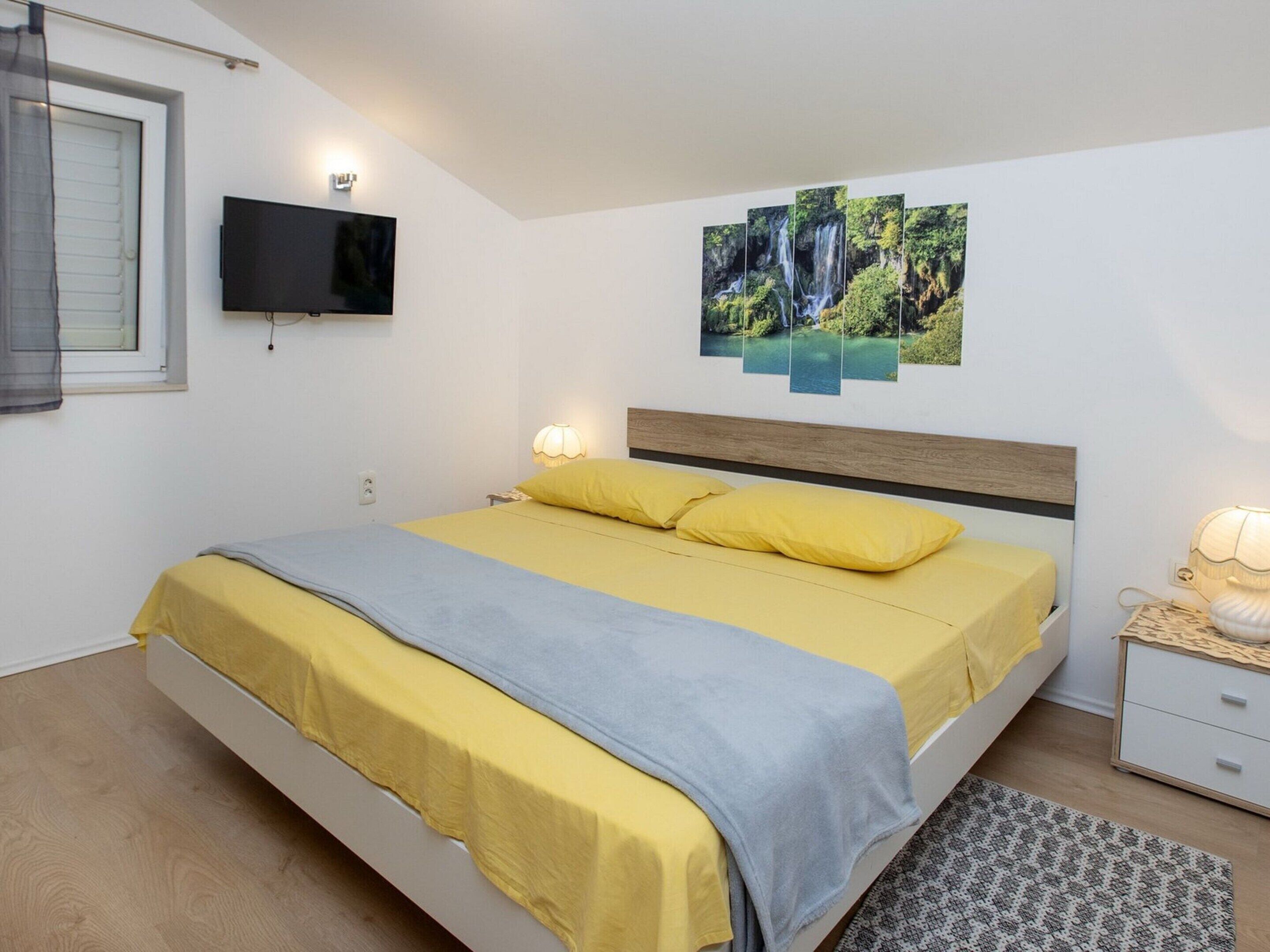 A bedroom with a bed, a TV mounted on the wall, and a painting of a waterfall.