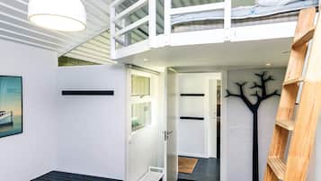 A modern loft bedroom with a bunk bed, a desk, and a ladder.