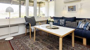 A room with a sofa, a table, a chair, a patterned rug, and a window with curtains.
