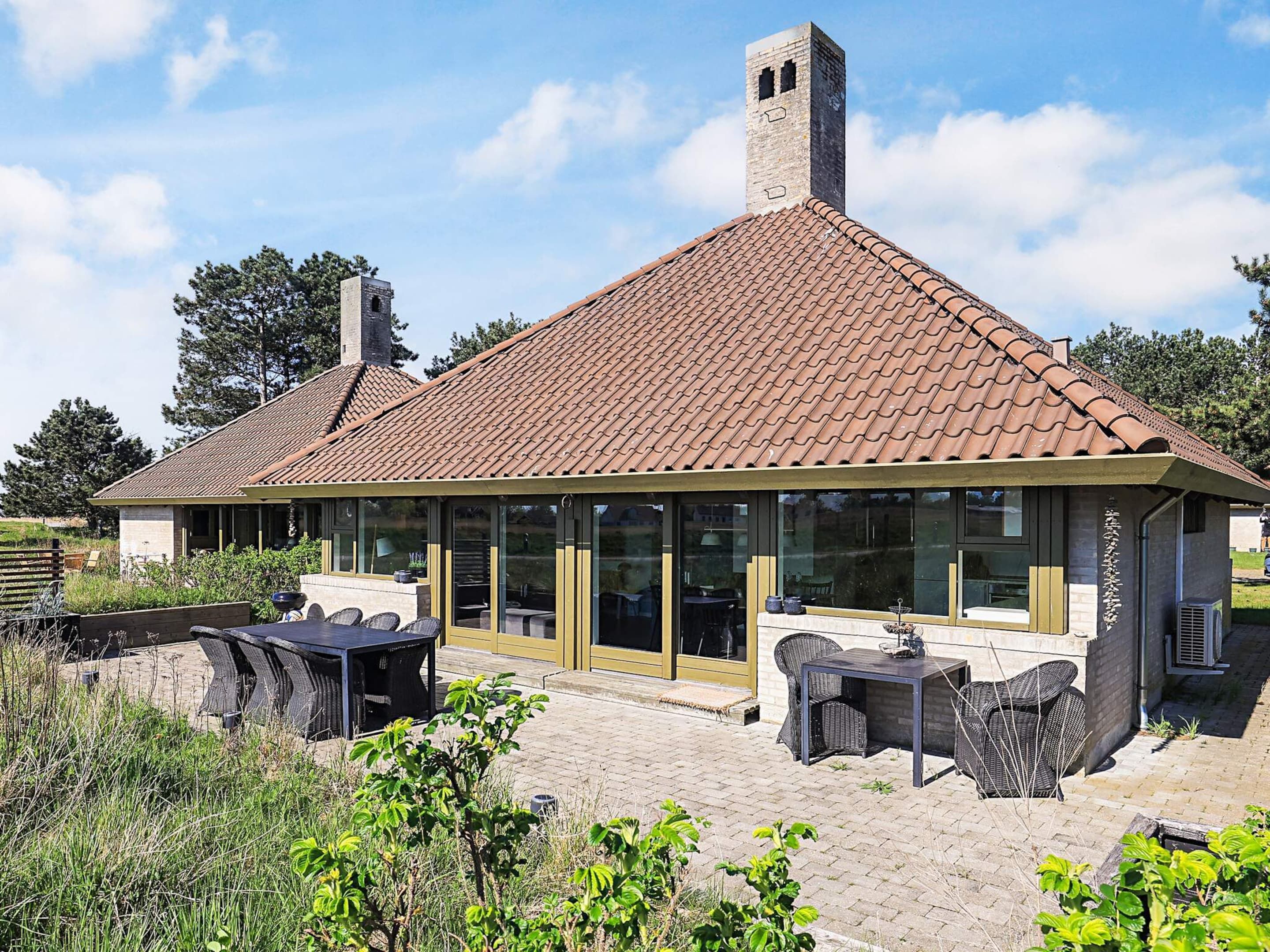 A house with a tiled roof, large glass windows, and outdoor seating.