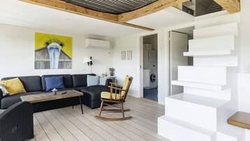 A modern living room with a sofa, a rocking chair, and a coffee table. There is a staircase with white steps and a wooden handrail.