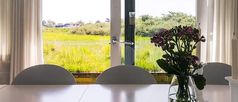 A dining area with a table, chairs, a vase with flowers, and a view of a green field through a glass door.