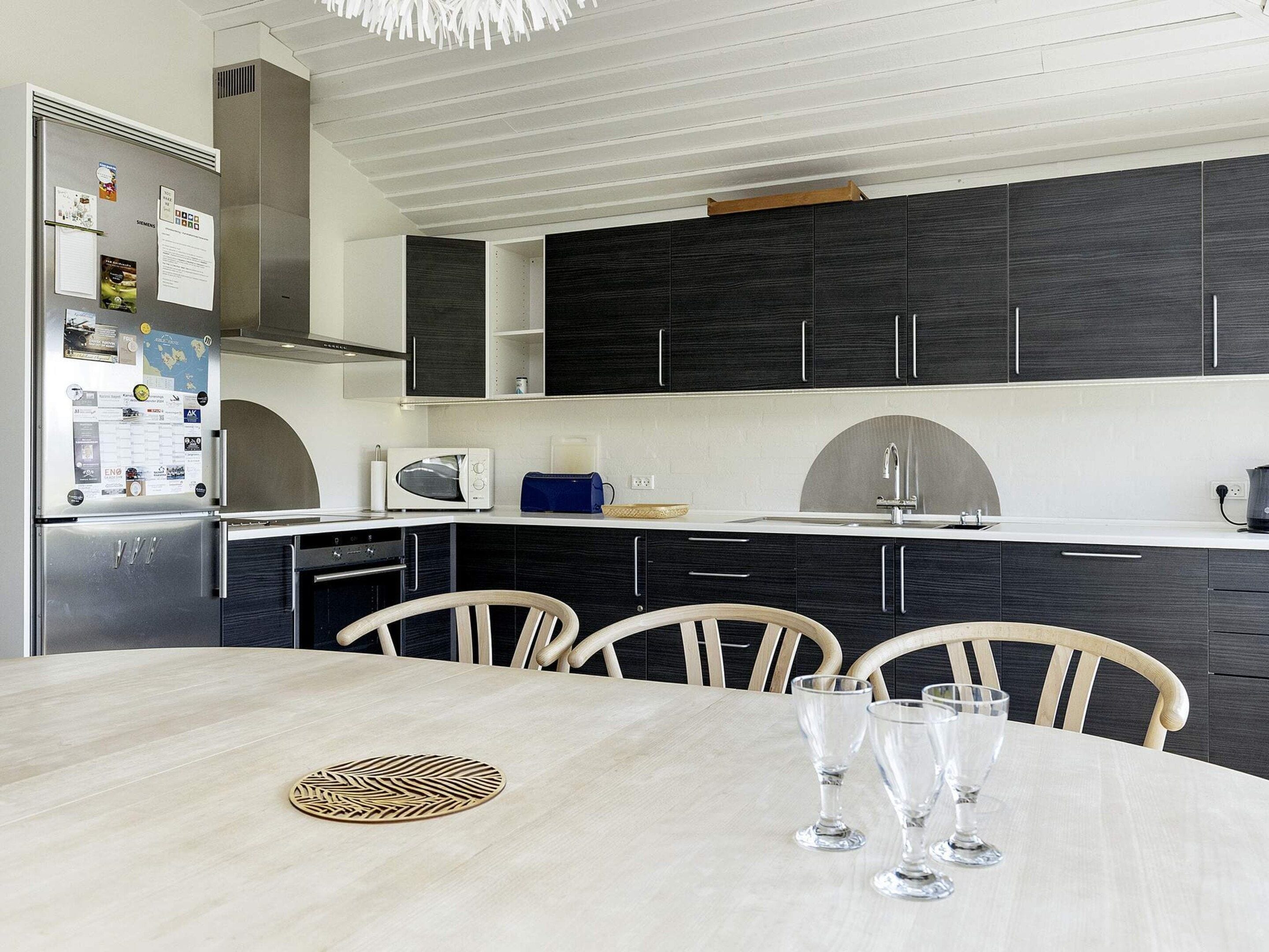 A modern kitchen with dark cabinets, a white countertop, and a dining table with chairs.