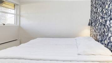 A neatly made bed with white bedding in a room with white walls and a window.