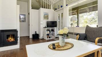 A modern living room with a fireplace, a dining table with a vase of flowers, a sofa, and a television.