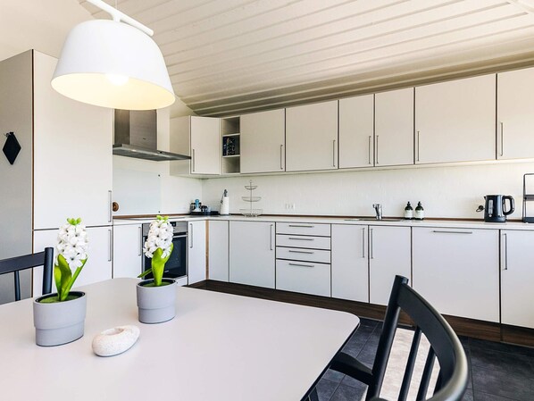Une cuisine moderne avec des meubles blancs, une table blanche et un luminaire suspendu.