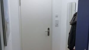 Un pasillo estrecho con una puerta blanca, un pequeño banco de madera y un armario azul.