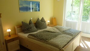 Un dormitorio con cama, dos mesitas de noche, una lámpara de noche, una ventana con persianas y un cuadro en la pared.