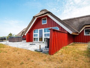A red barn-style building with a thatched roof, large windows, and a paved patio area. - 12 Person Holiday Home in Romo (Rømø)