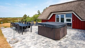 A patio area with a table and chairs, a hot tub, and a red building with a thatched roof.