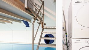 A laundry area with a washing machine and a metal ladder leading to a blue pipe.